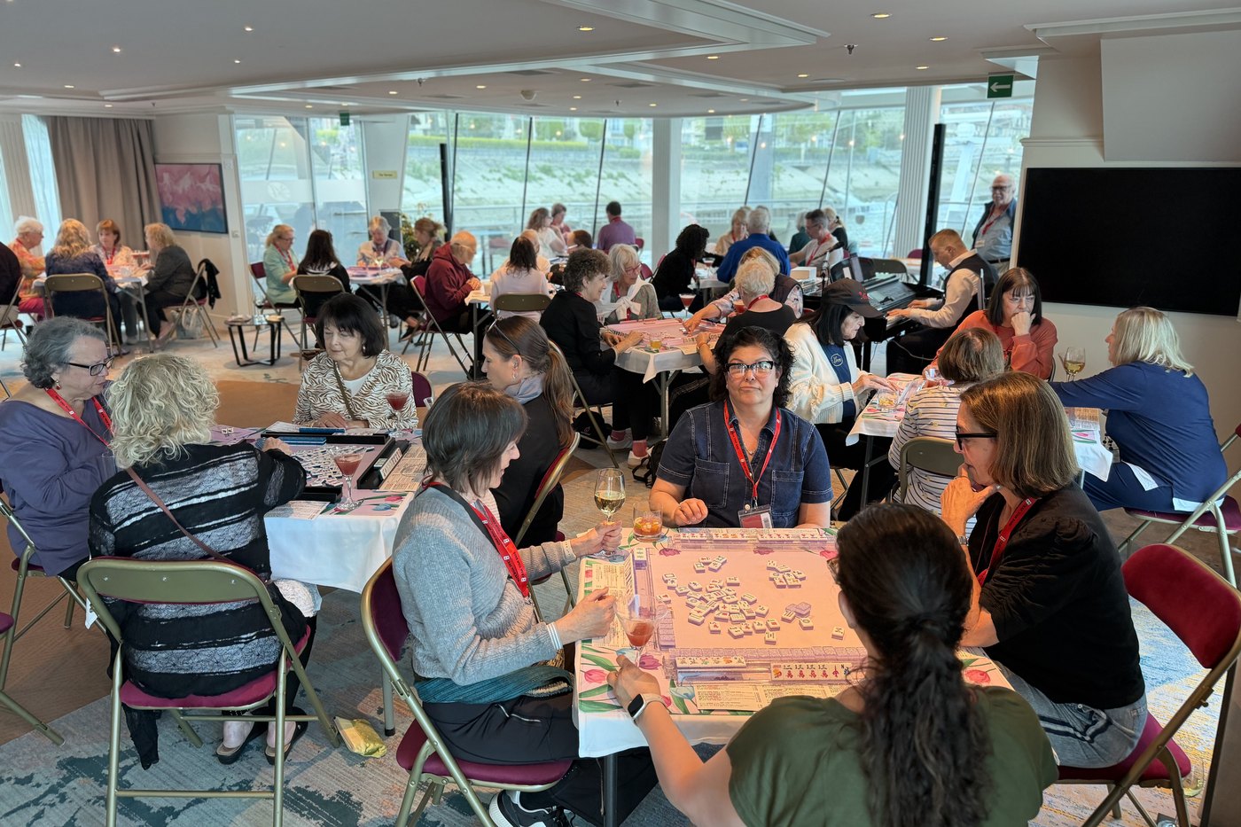 A room full of Mah Jongg tables in play aboard the ship, the river through the windows behind